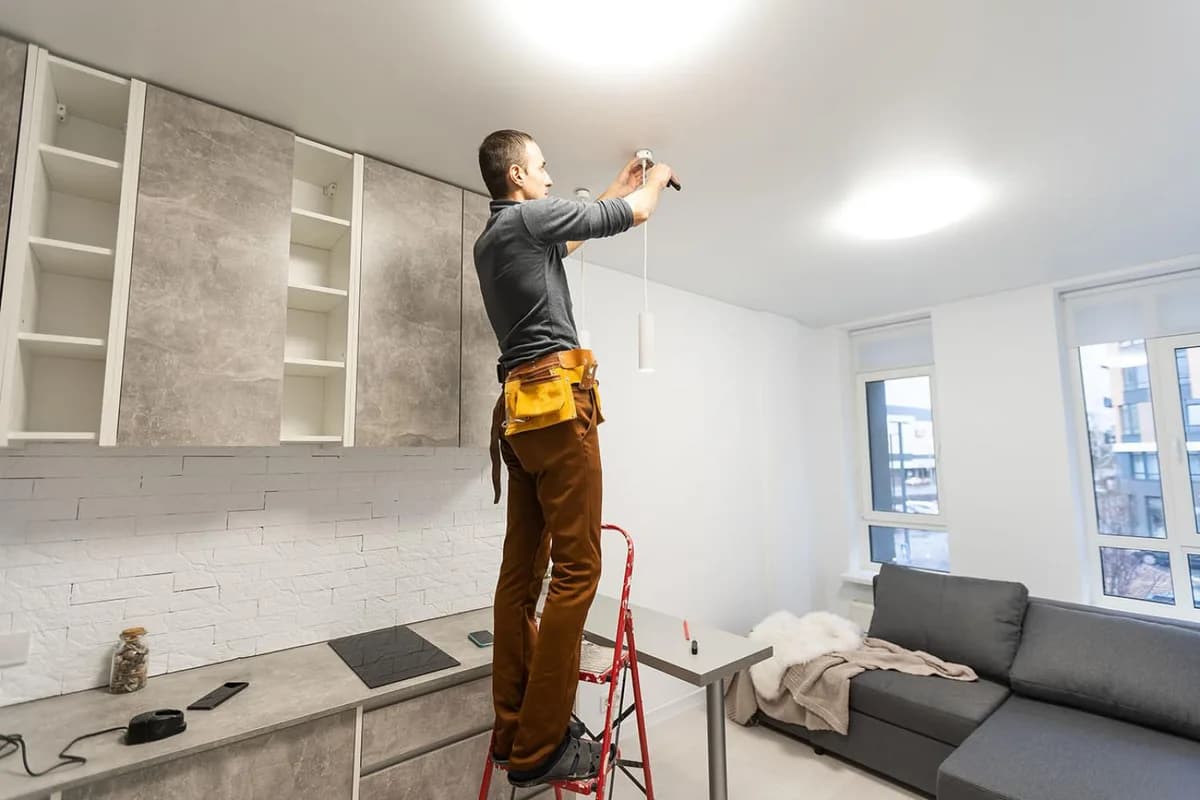 Elektriker på stege monterar takbelysning i en nyrenoverad lägenhet