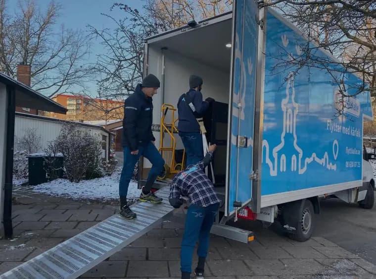 Flyttare bär tunga möbler uppför en ramp in i en flyttbil